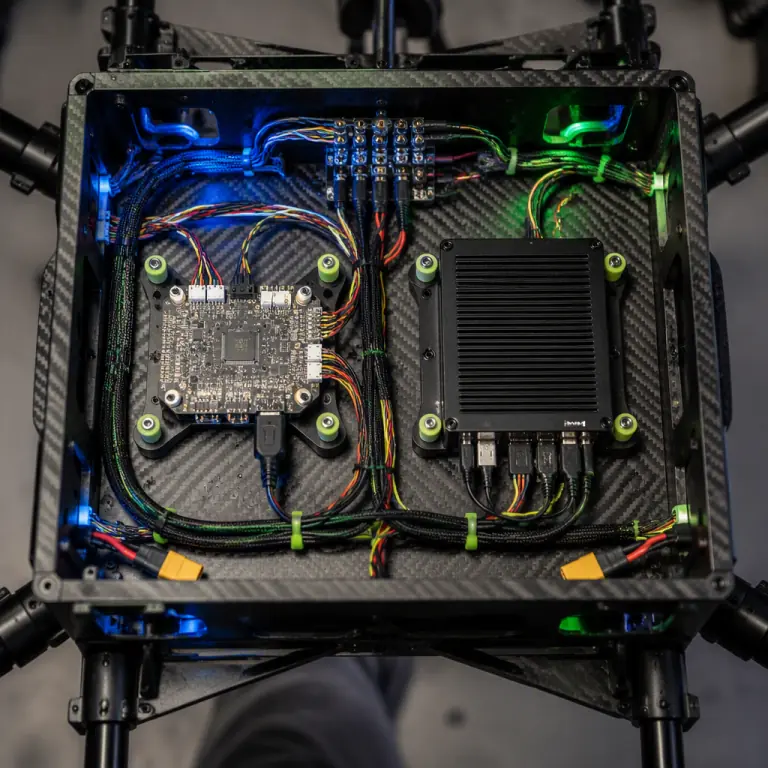 Top-down photograph of a UAV avionics tray holding a flight controller and a compact companion computer mounted on small metal-laminate vibration isolators, neatly routed wiring with service loops, dark carbon fiber deck, blue and lime-green accent lighting, photorealistic, no people faces, no text, no logos